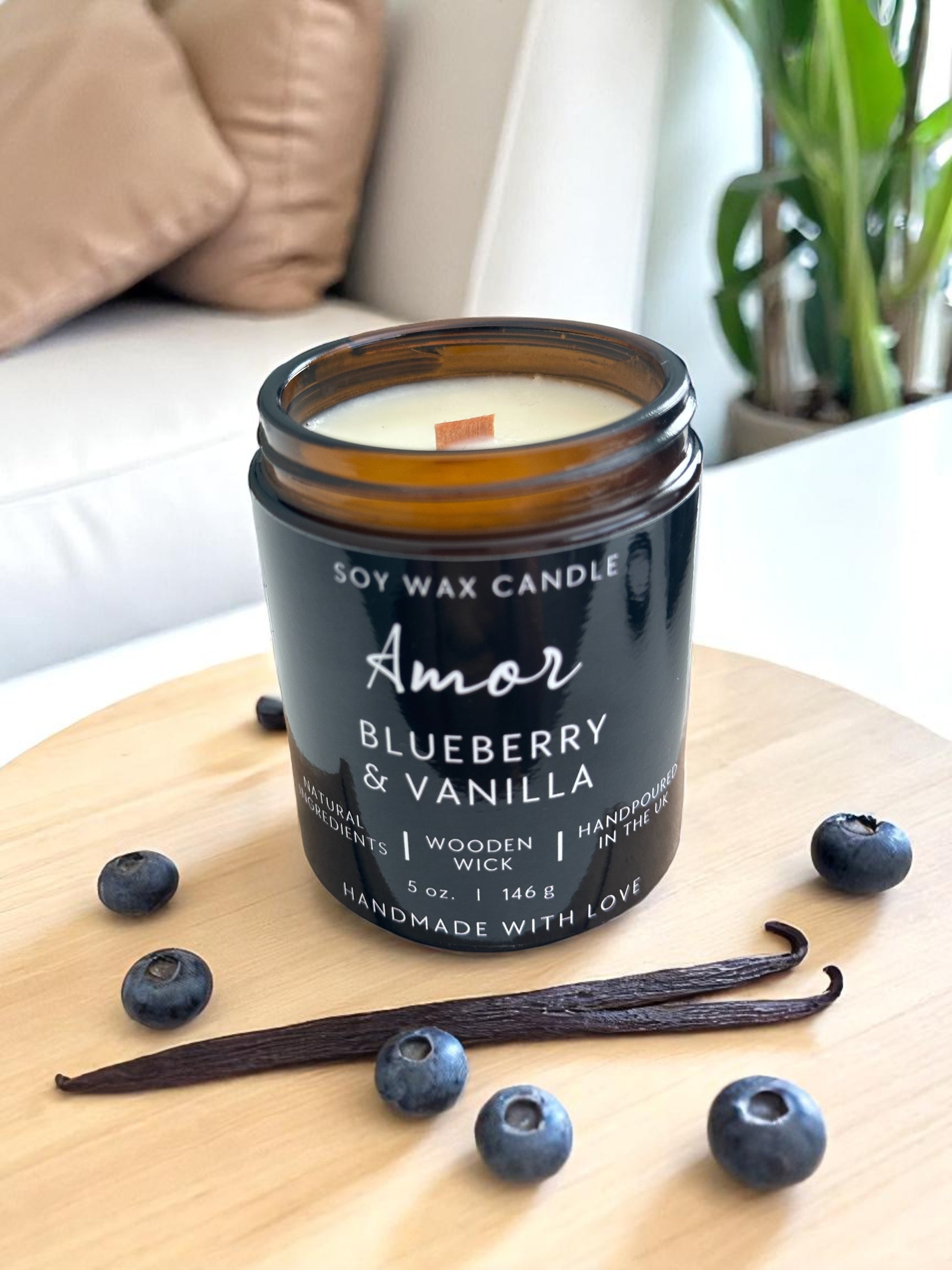 Soy wax candle labeled 'Amor' with blueberries and vanilla beans on a wooden surface.