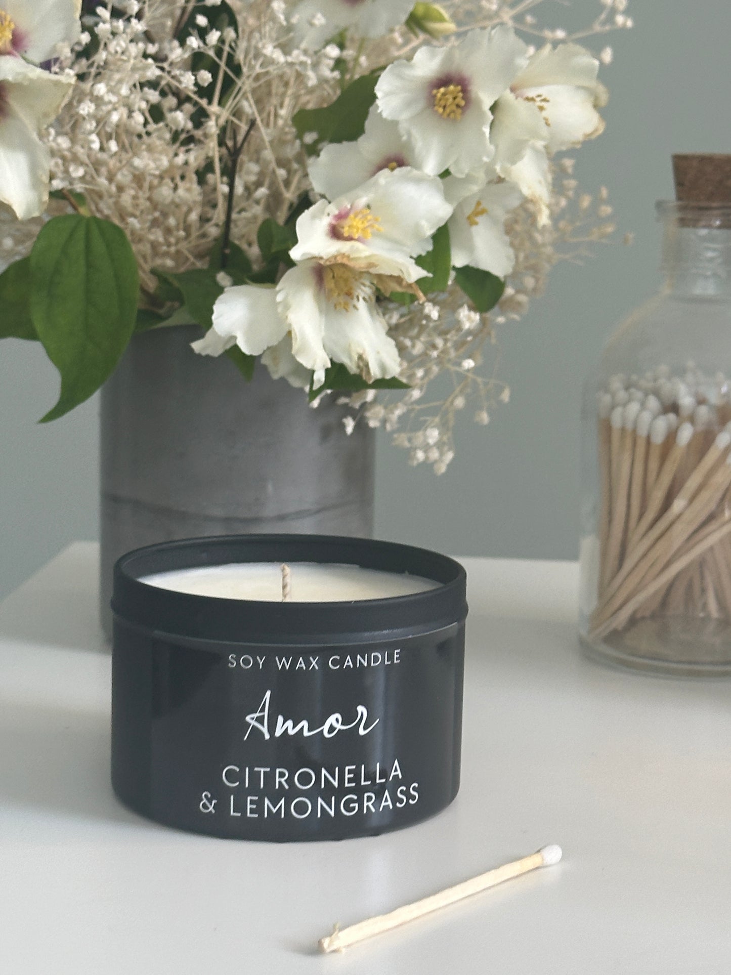 Candle labeled 'Amor' with flowers and matches on a surface