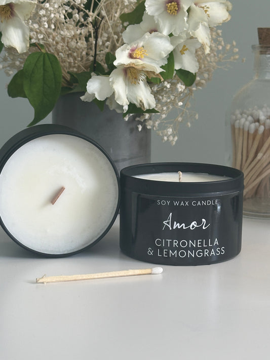 Candle with a black lid labeled 'Amor' next to white flowers on a gray surface
