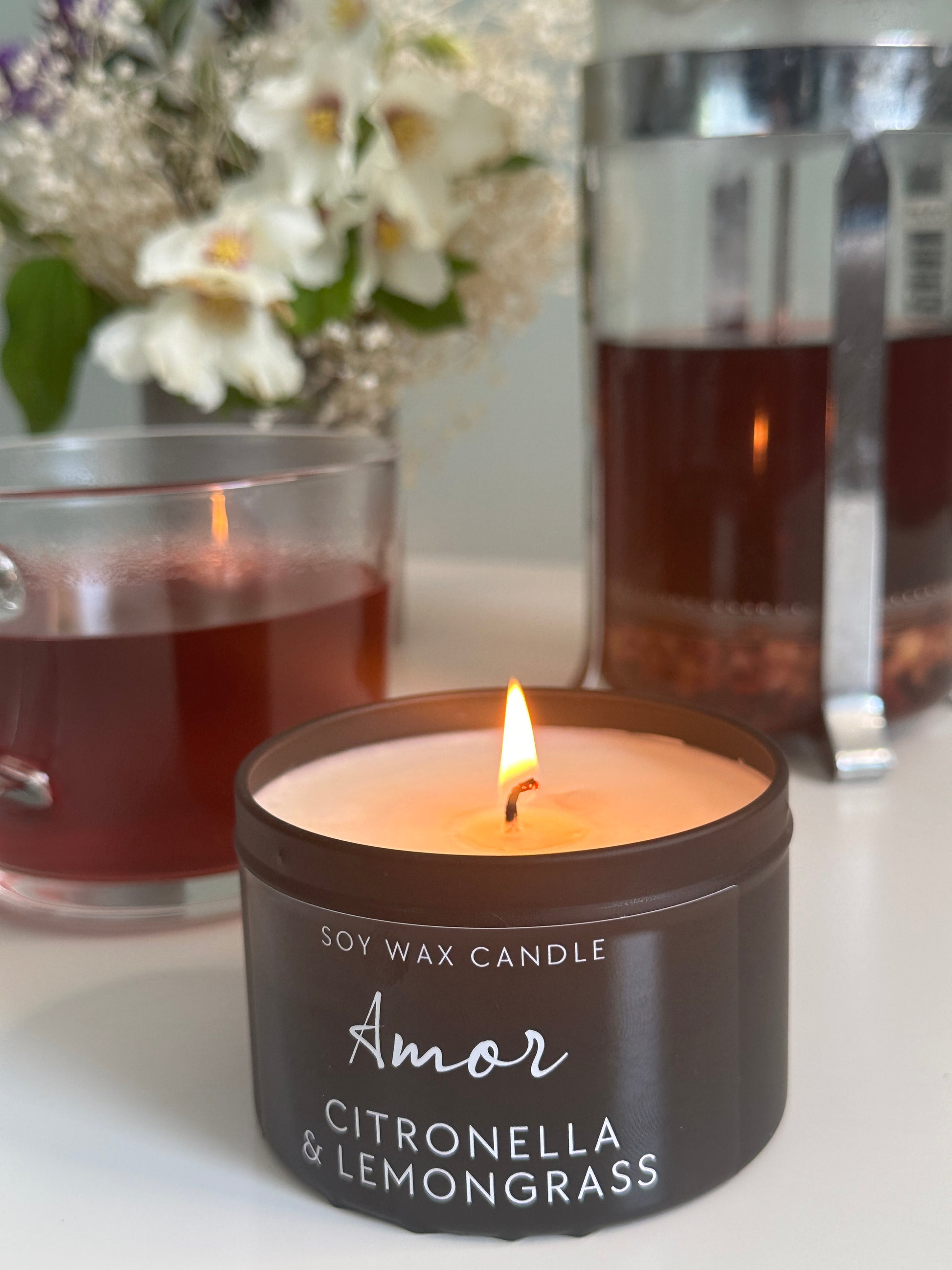 Amor Citronella & Lemongrass candle burning with a blurred background