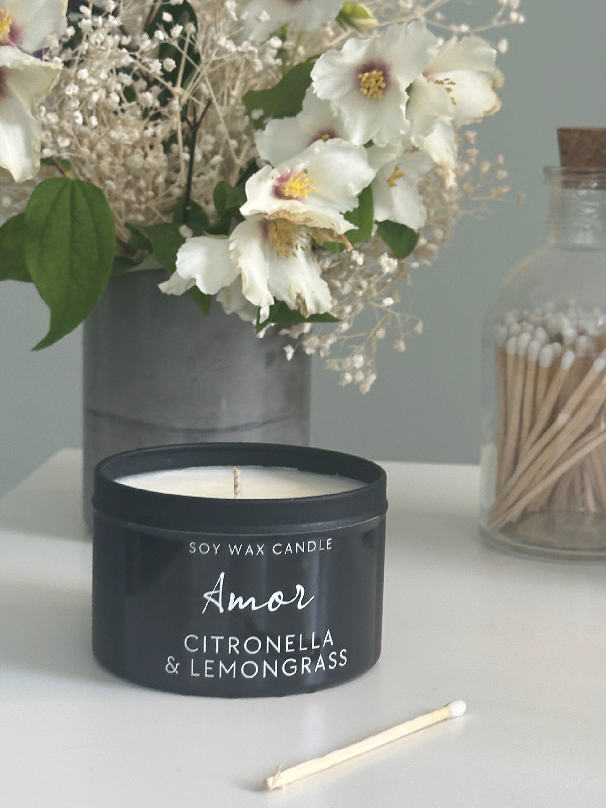 Candle labeled 'Amor' with flowers and matches on a surface