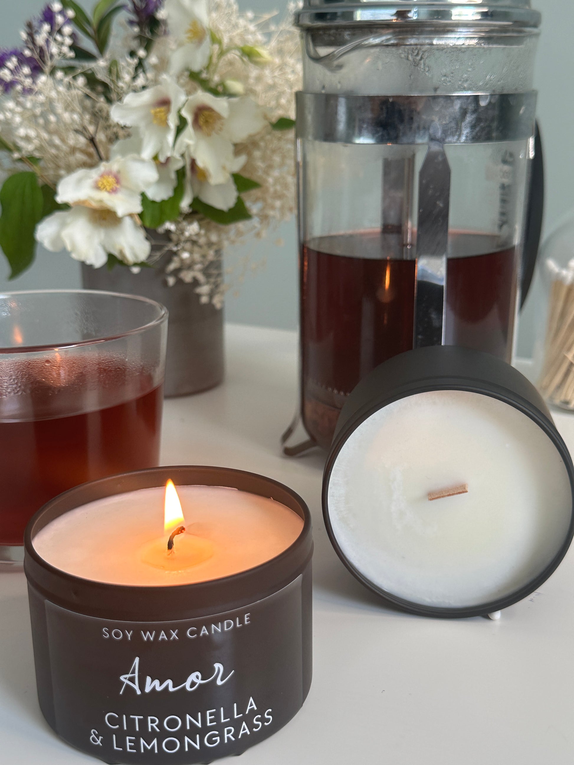 Two lit candles with floral arrangement on a white surface