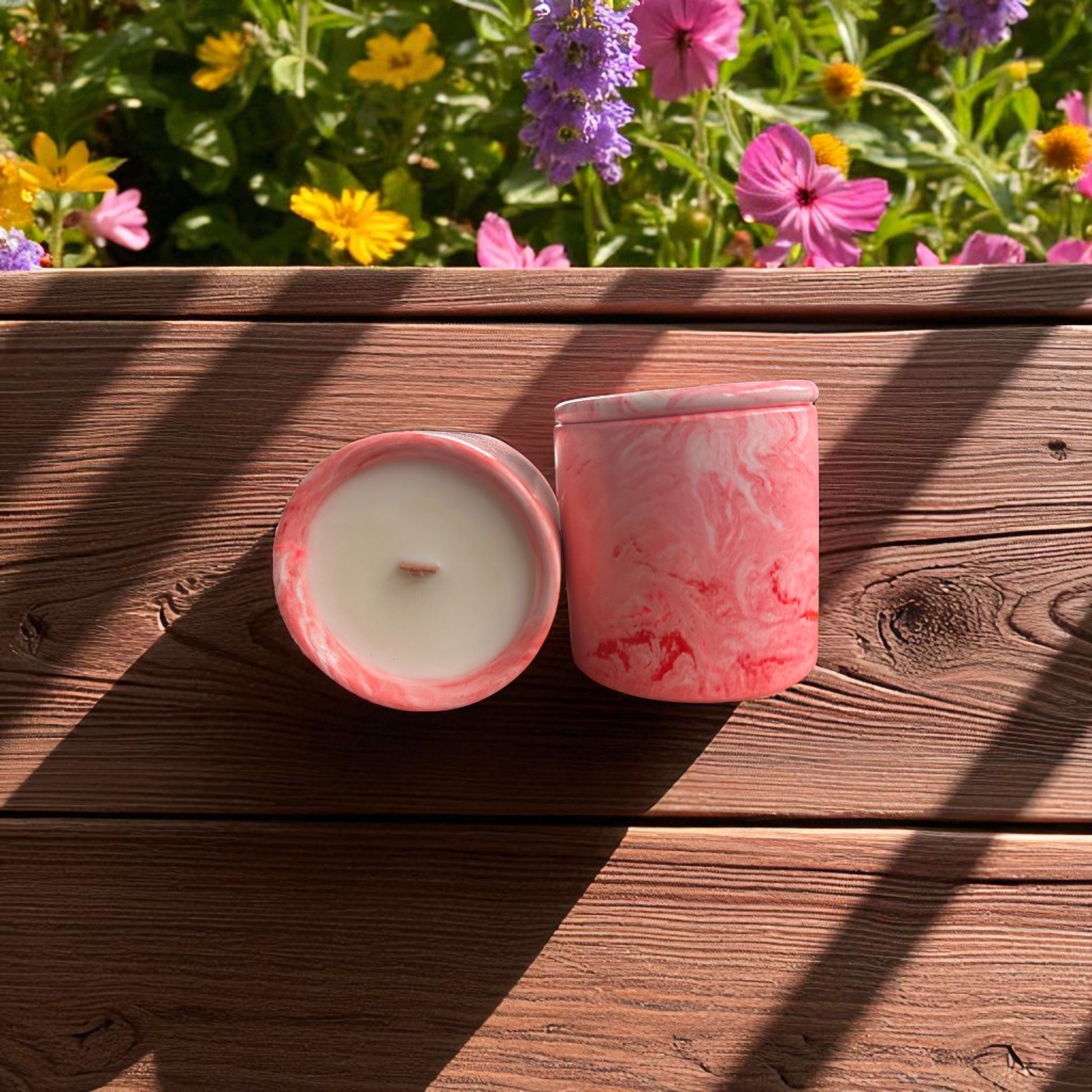 Pink marbled candles on a wooden surface with flowers in the background