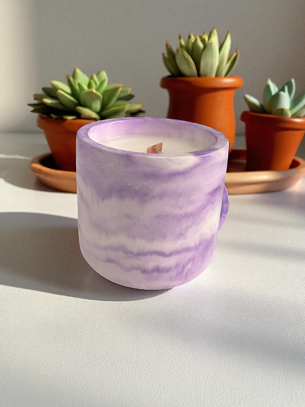 Purple marbled candle on a white surface with potted succulents in the background