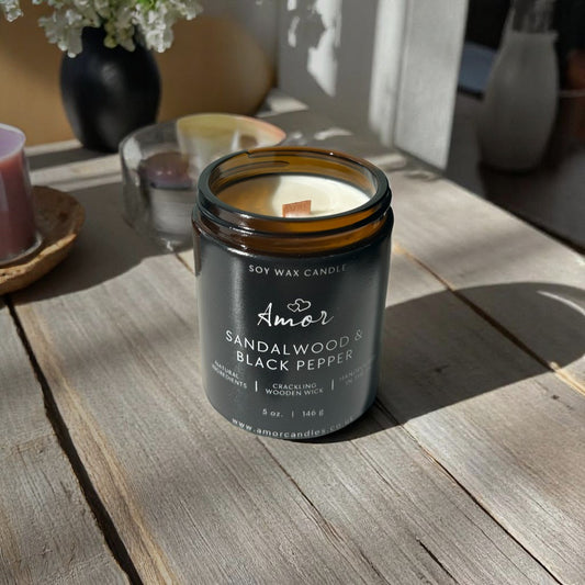 Sandalwood & Black Pepper candle in a glass jar on a wooden table with a blurred background