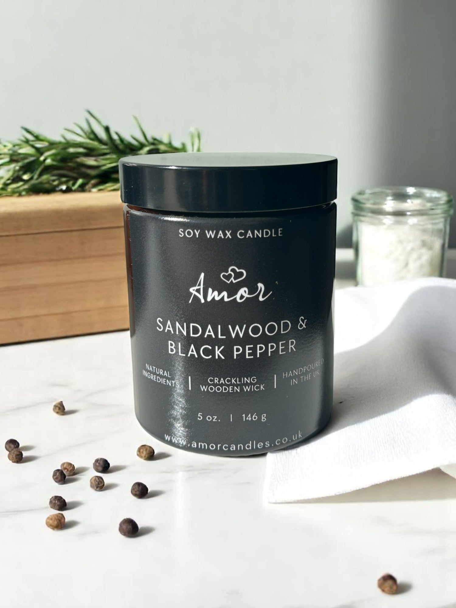 Sandalwood & Black Pepper candle by Amor on a white surface with black pepper and sandalwood.