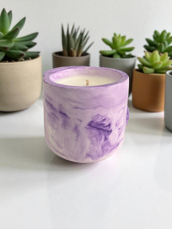 Purple marbled candle on a white surface with potted plants in the background
