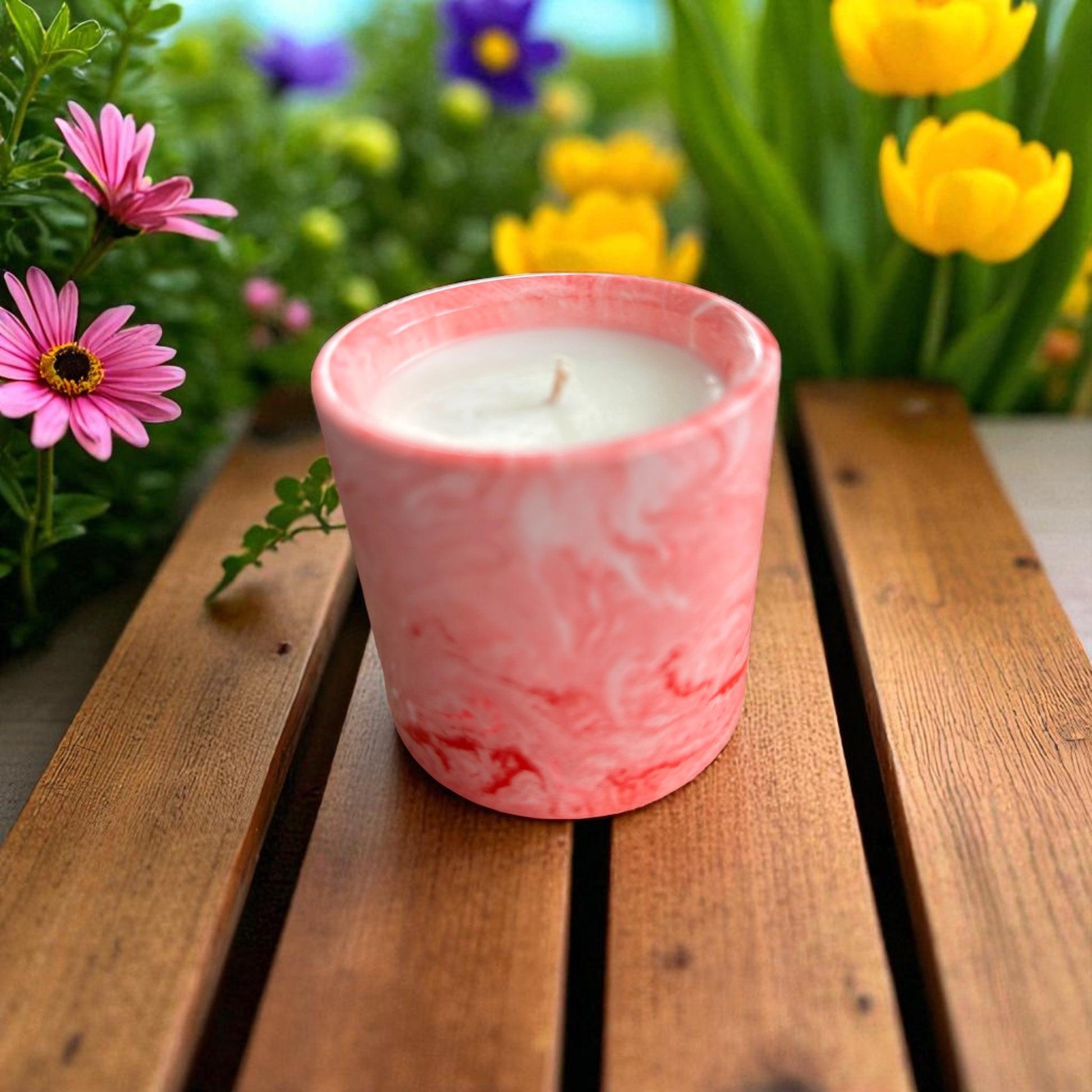 Pink marbled candle on a wooden surface with flowers in the background